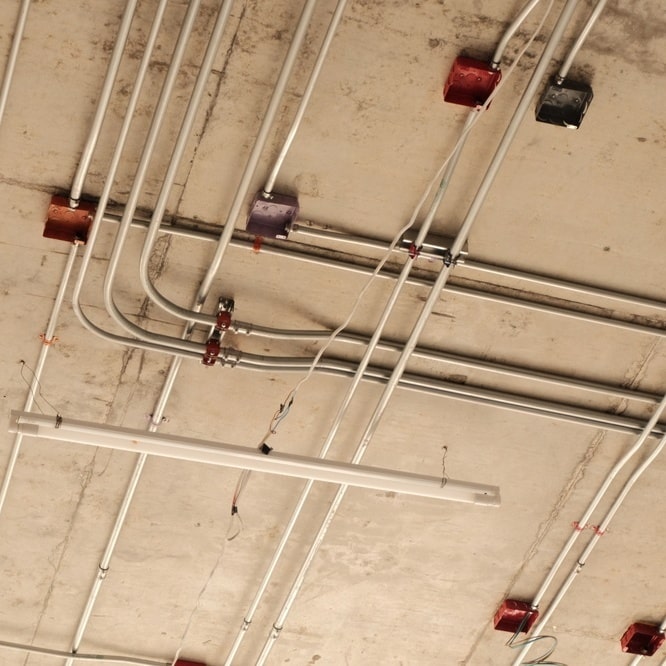 Installation de Conduits Électriques sur Plafond Béton Réseau de conduits électriques et boîtes de dérivation colorées sur un plafond en béton brut industriel.